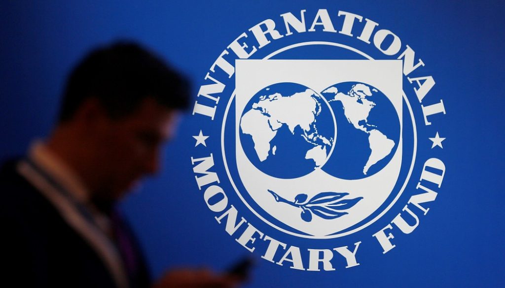 A participant stands near a logo of IMF at the International Monetary Fund - World Bank Annual Meeting 2018 in Nusa Dua